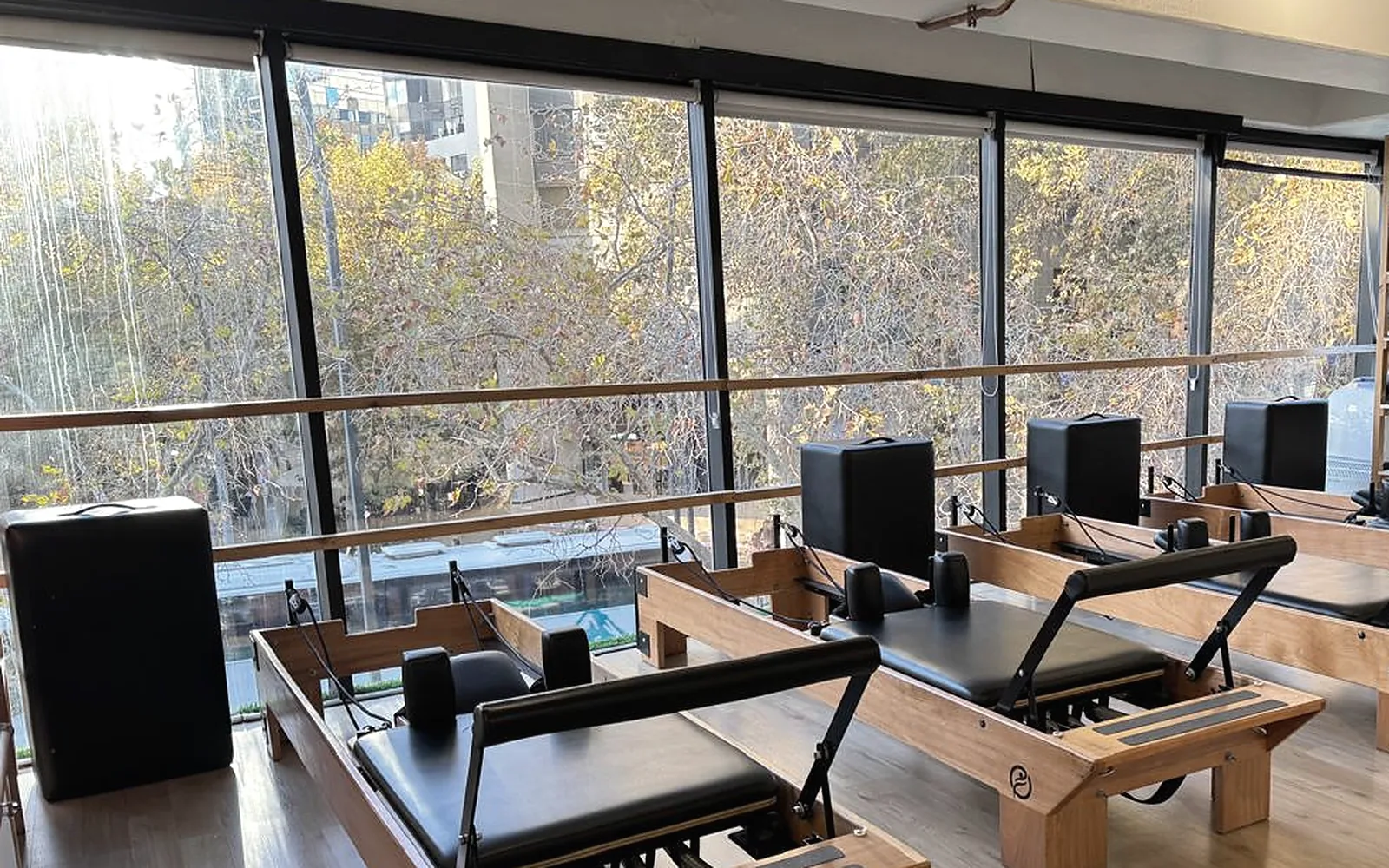 Sala de Enjoy Pilates con reformers de madera frente a un ventanal con árboles, en Providencia